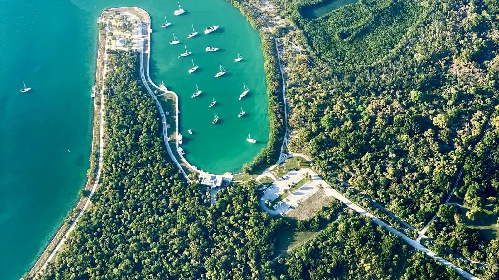 Aerial view of a mangrove-fringed cove with small boats anchored in shallow green water
