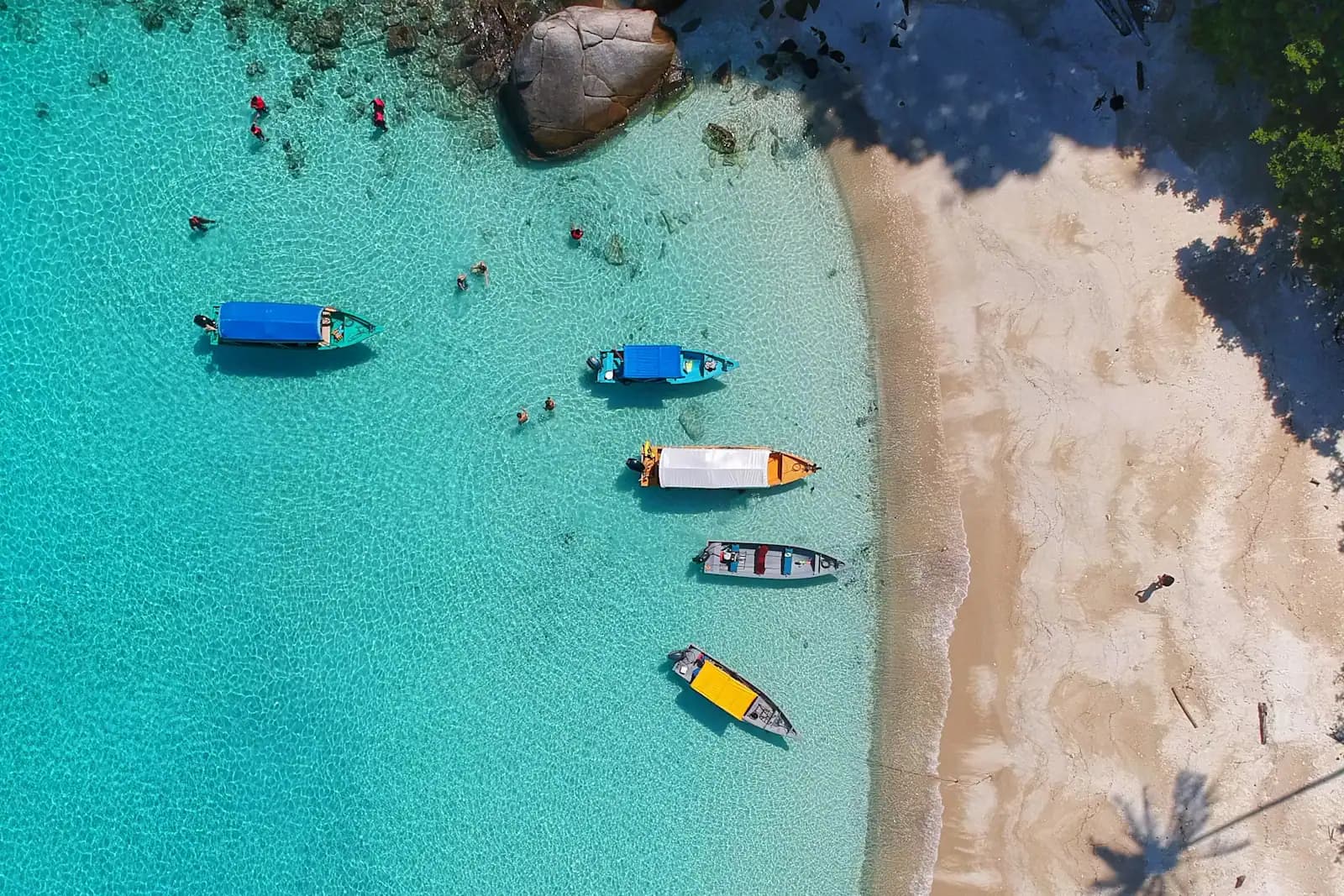 Small boats moored in clear shallow water beside a pale sandbank, seen from above