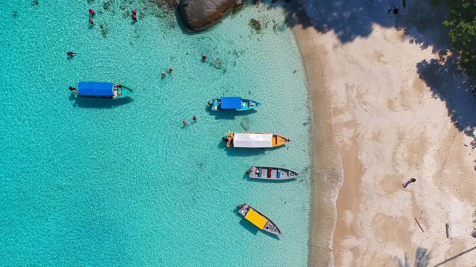 Small boats on shallow clear water beside a sandbar, seen from above