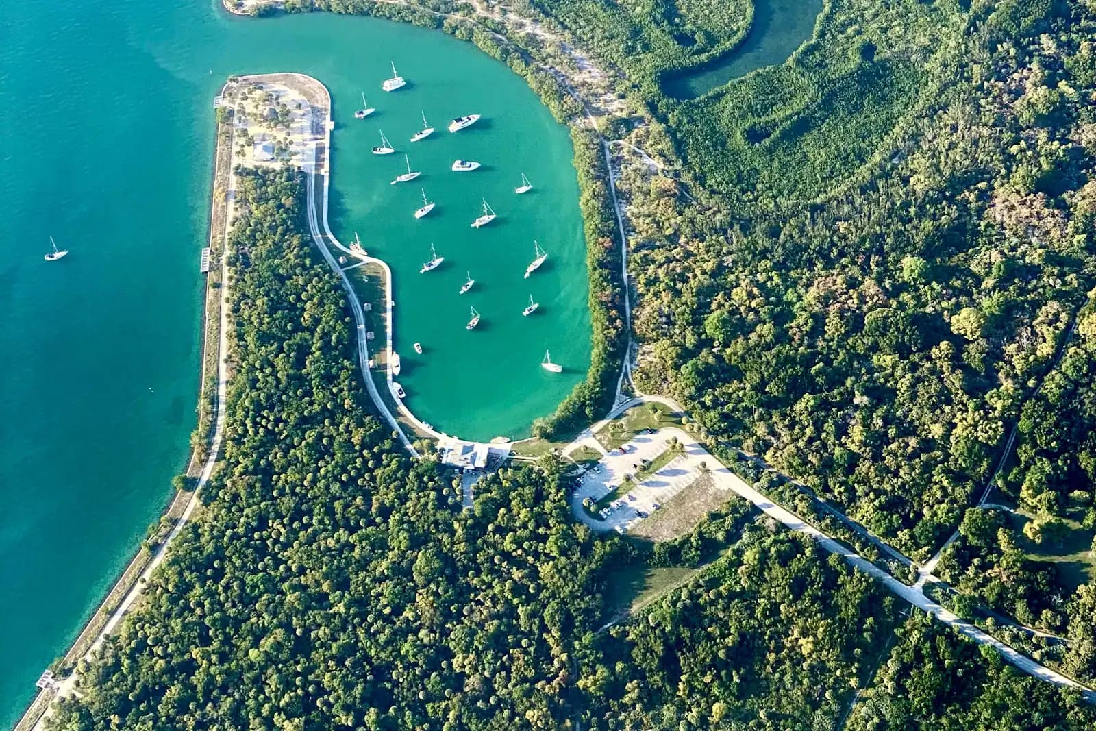 Aerial view of a mangrove-fringed cove with boats anchored in shallow green water