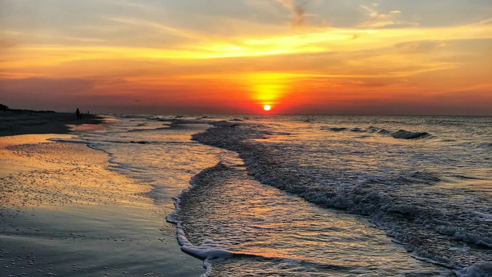 The sun dropping into open water beyond low surf on a wide Gulf beach