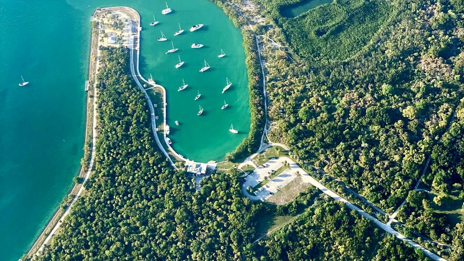 Aerial view of a mangrove-fringed cove with small boats anchored in shallow green water