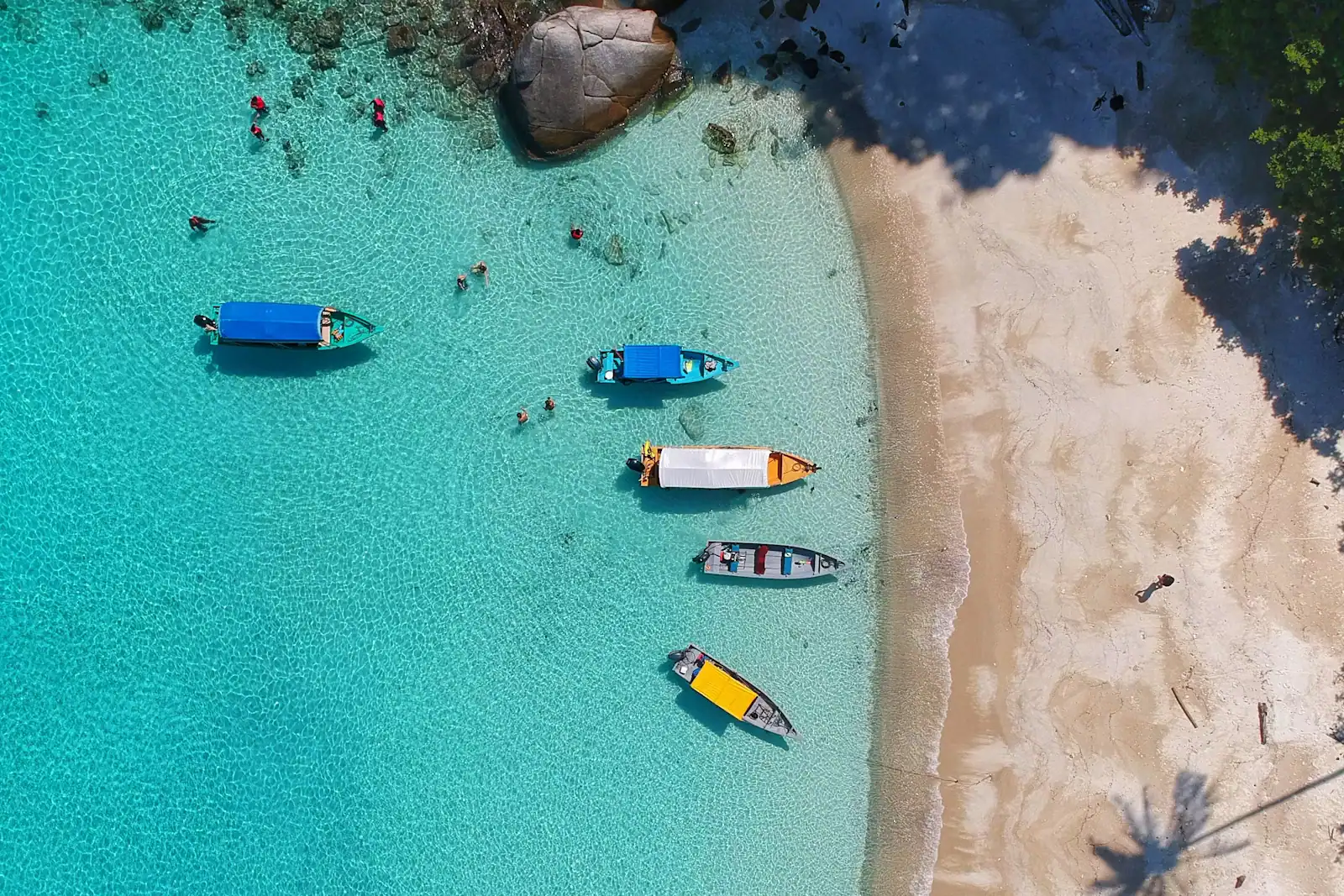 Small boats moored in clear shallow water beside a pale sandbank, seen from above