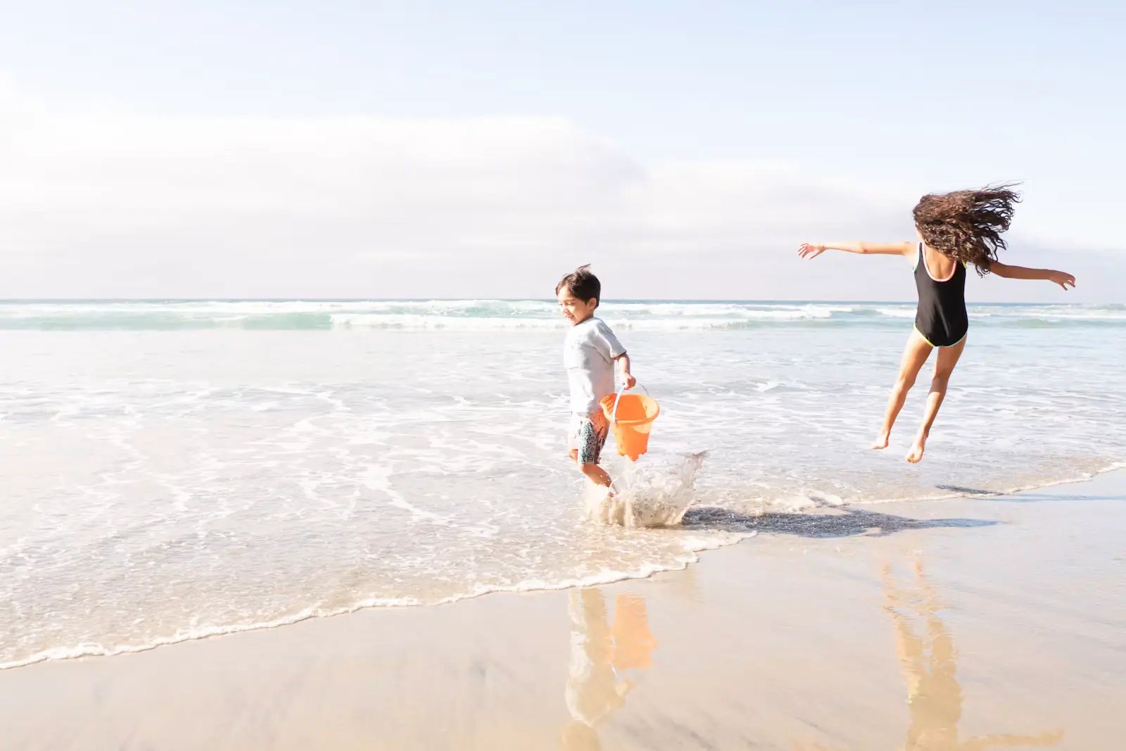 Two children running along wet sand at the edge of shallow water