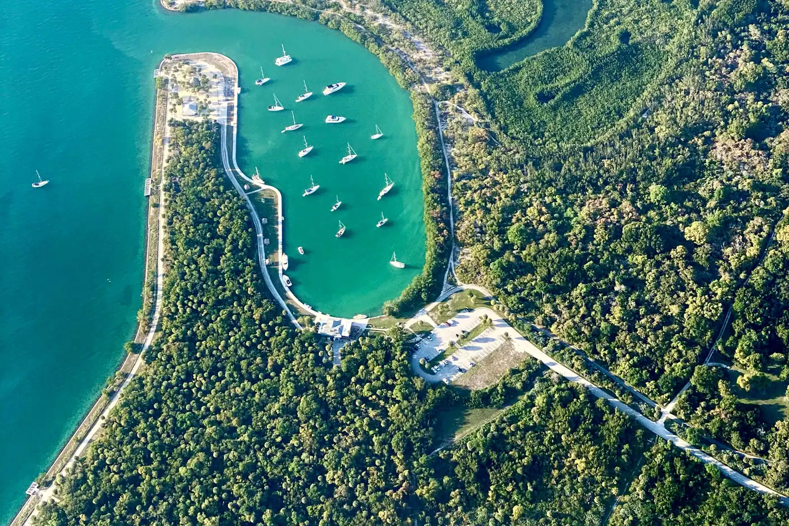 Aerial view of a mangrove-fringed cove with boats anchored in shallow green water