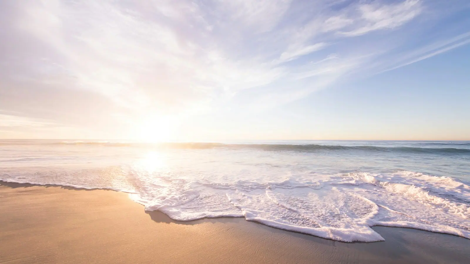 Low sun over a wide, pale Gulf beach with a thin line of foam running up flat sand