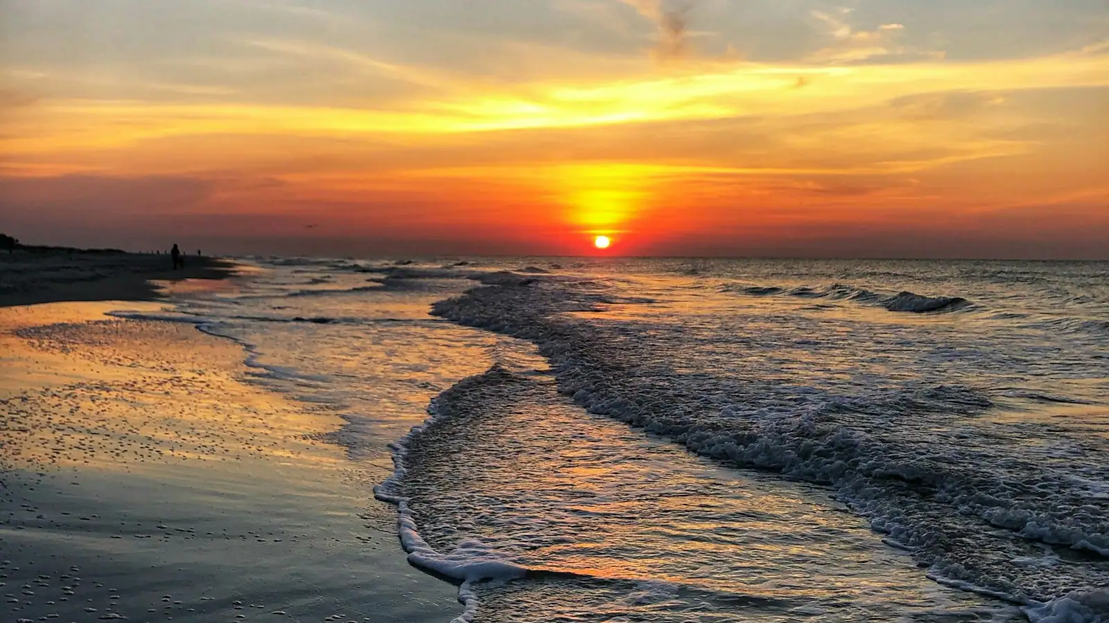 The sun dropping into open water beyond low surf on a wide Gulf beach